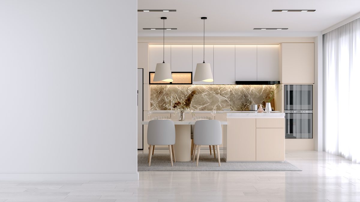 A pale kitchen with two white pendant lights over a small round table, slim recessed ceiling lights and a marble splashback